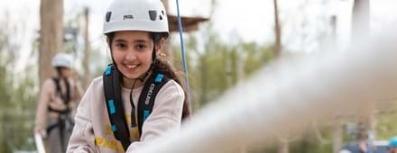 meisje lacht in camera tijdens klimmen bij outdoor klimpark Adventure City Rotterdam