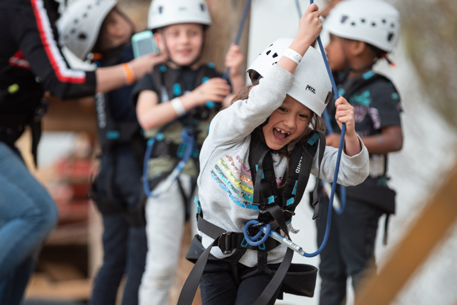 meisje heeft plezier en lacht tijdens klimmen bij outdoor klimpark Adventure City Rotterdam